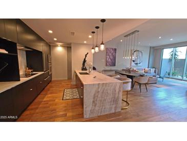 Modern kitchen boasts stone countertops, pendant lighting, stainless appliances, and open layout to the living room at 5455 E Lincoln Dr # 1004, Paradise Valley, AZ 85253