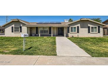 Charming single-story home with a well-manicured lawn, solar panels, and inviting front porch at 624 N Ashbrook Cir, Mesa, AZ 85213