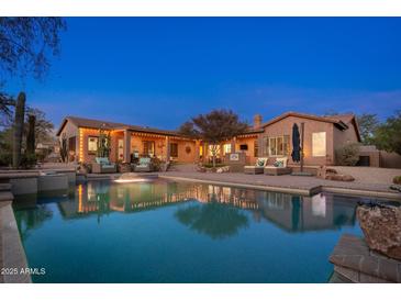 A stunning backyard oasis featuring a pool, outdoor seating, and beautifully lit landscaping at twilight at 5712 E Blue Sky Dr, Scottsdale, AZ 85266