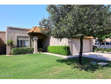 Charming home with a well-maintained lawn, lush green shrubs, and an attached two-car garage at 9419 E Riviera Dr, Scottsdale, AZ 85260