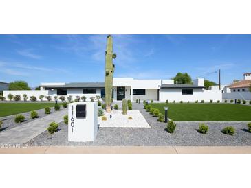 Stunning modern home featuring desert landscaping with a tall saguaro cactus and a well-manicured lawn at 11601 N 64Th Pl, Scottsdale, AZ 85254