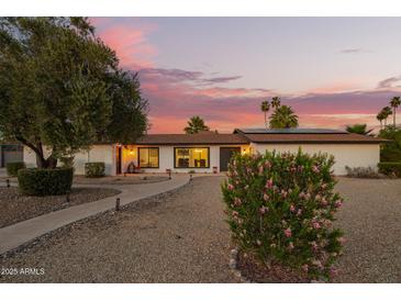 Charming single-story home featuring a lush, landscaped yard and inviting walkway under a beautiful sunset sky at 12866 W Orange Dr, Litchfield Park, AZ 85340