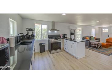 Open kitchen featuring stainless steel appliances, white cabinets, black counters, and light wood flooring at 520 S Macdonald --, Mesa, AZ 85210