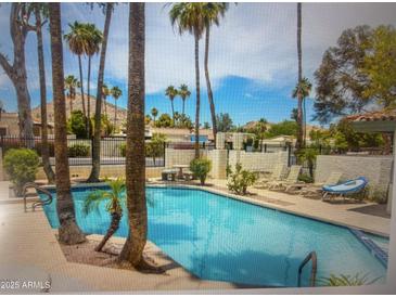 Community swimming pool with palm trees, lounge chairs, tables, and mountain views in a gated area at 8653 S 51St St # 2, Phoenix, AZ 85044