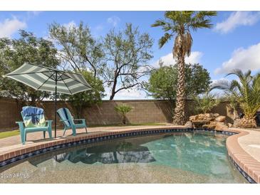 Backyard pool with a stone waterfall, lush landscaping, and two chairs under an umbrella at 21362 E Puesta Del Sol Rd, Queen Creek, AZ 85142