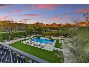 Inviting pool area with luxurious lounge chairs, lush landscaping, and beautiful mountain views at dusk at 9939 E Desert Jewel Dr, Scottsdale, AZ 85255