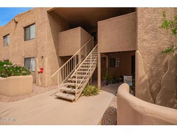 Exterior view of a tan building with concrete walkway and staircase leading to upper level condos in a lush landscape at 8155 E Roosevelt St # 205, Scottsdale, AZ 85257