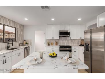 Bright kitchen features white cabinetry, stainless steel appliances, and a marble countertop island at 10625 E Bramble Ave, Mesa, AZ 85208