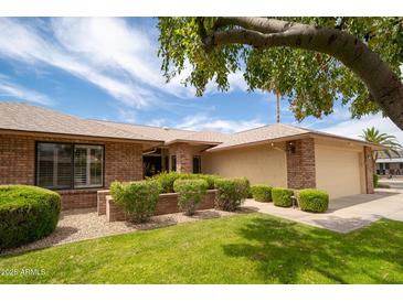 Charming single-story brick home featuring a well-manicured lawn, mature trees, and an attached two-car garage at 13055 W Tangelo Dr, Sun City West, AZ 85375