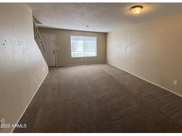 Inviting living room featuring neutral walls, carpet, and natural light from the window and a stairway to the upper level at 7126 N 19Th Ave # 108, Phoenix, AZ 85021