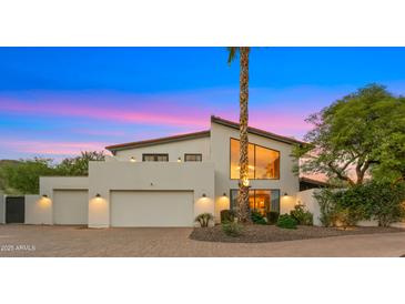 Striking two-story home with a three-car garage and mature landscaping against a colorful dusk sky at 4824 E Hummingbird Ln, Paradise Valley, AZ 85253