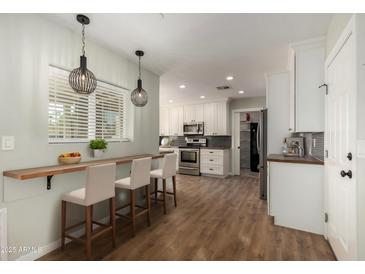 Bright kitchen featuring white cabinets, stainless steel appliances, breakfast bar and stylish pendant lighting at 4939 E Paradise Dr, Scottsdale, AZ 85254
