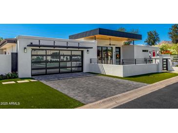 Modern home exterior featuring a glass garage door, gray brick driveway, and manicured lawn at 5822 N 44Th Pl, Phoenix, AZ 85018