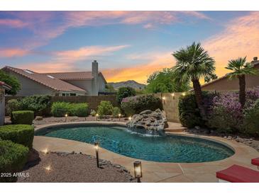 A stunning pool with a rock waterfall feature surrounded by lush landscaping and a captivating sunset sky at 4428 E Yawepe St, Phoenix, AZ 85044