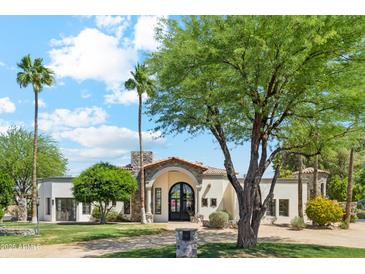 Elegant home with a well-manicured lawn, mature trees, and a grand entrance with arched doorway and a stone accent chimney at 5402 E Cortez Dr, Scottsdale, AZ 85254