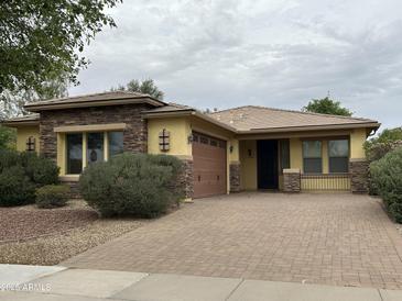 Charming single-story home with a brick driveway, manicured shrubs and stone accents around the windows at 16528 W Lariat Ln, Surprise, AZ 85387
