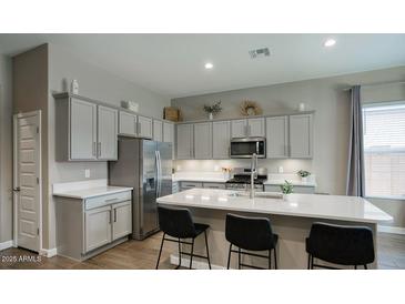 A modern kitchen featuring an island with bar seating, stainless steel appliances, and shaker style cabinets at 40816 W Sunland Dr, Maricopa, AZ 85138