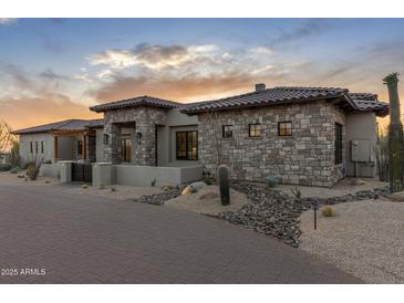 Stunning stone-clad exterior with desert landscaping and a paver driveway, showcasing elegant design and curb appeal at 9456 E Sands Dr, Scottsdale, AZ 85255