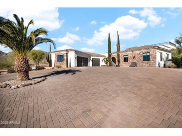Stunning home featuring a stone and stucco exterior, a spacious brick driveway, and mature desert landscaping with palm trees at 13648 E Aloe Vera Dr, Scottsdale, AZ 85262
