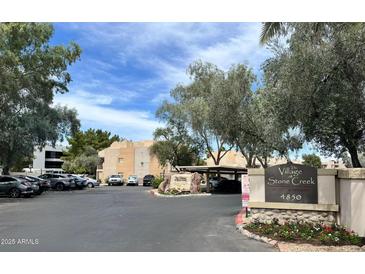 View of the The Village at Stone Creek sign with lush trees and landscaping, with community buildings and parking visible at 4850 E Desert Cove Ave # 241, Scottsdale, AZ 85254