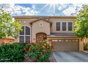 Two-story home with a tan stucco exterior, tile roof, attached garage, and vibrant orange flowering bushes at 3025 N Desert Horizons Ln, Casa Grande, AZ 85122