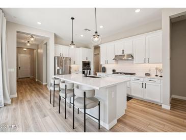 Bright, white kitchen with modern appliances, a large island with seating, and wood-look floors at 1865 N 141St Ave, Goodyear, AZ 85395