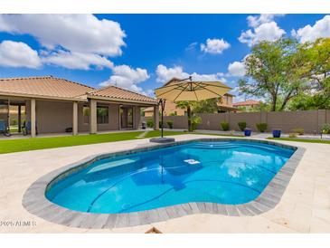 Inviting backyard pool with lounge umbrella, lush landscaping, and a beautiful blue sky at 2111 E Yellowstone Pl, Chandler, AZ 85249