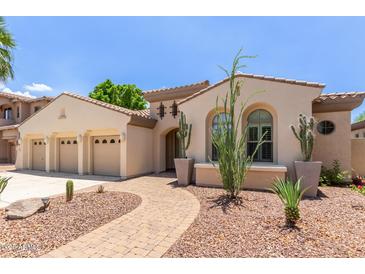 Elegant stucco home showcasing a three-car garage, desert landscaping, and a charming arched entryway at 915 W Orchard Ln, Litchfield Park, AZ 85340