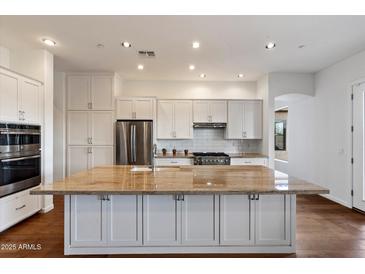 Bright white kitchen featuring stainless steel appliances, a large island with granite countertops, and hardwood floors at 5832 E Bent Tree Dr, Scottsdale, AZ 85266