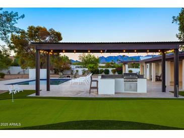 Outdoor kitchen with stainless steel grill, and a pergola with lights near a pool and putting green at 13620 N 80Th Pl, Scottsdale, AZ 85260