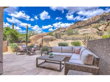 Inviting stone patio featuring a wicker sectional, lounge chairs, and stunning desert mountain views at 25555 N Windy Walk Dr # 69, Scottsdale, AZ 85255