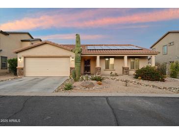 Charming single-story home featuring desert landscaping, a two-car garage, and solar panels on the roof at 2487 S Conestoga Rd, Apache Junction, AZ 85119