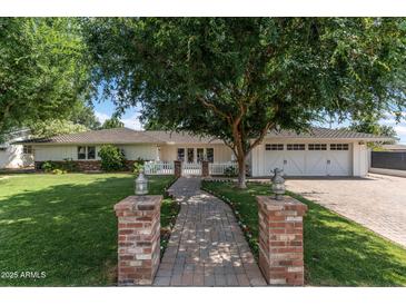 Charming home featuring a brick walkway, lush lawn, white picket fence, and large tree, with a two-car garage at 3817 E Highland Ave, Phoenix, AZ 85018