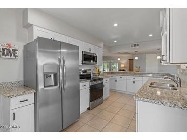 Bright kitchen featuring stainless steel appliances, granite countertops, and white cabinetry at 10895 W Clair Dr, Sun City, AZ 85351