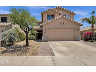Tan two-story home featuring a two-car garage, desert landscaping, and a brick paver walkway to the front door at 25409 N 40Th Ln, Phoenix, AZ 85083