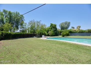 Relaxing backyard featuring a pool, lush green grass, mature trees, and ample privacy, perfect for outdoor entertaining at 325 W Loma Ln, Phoenix, AZ 85021