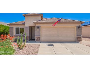 Charming single-story home featuring a two-car garage, desert landscaping, and an American flag at 22543 W Cocopah St, Buckeye, AZ 85326