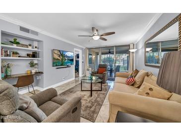 Open-concept living room with tile flooring, ceiling fan, built-in shelves, and sliding glass doors to the patio at 7625 E Camelback Rd # B138, Scottsdale, AZ 85251