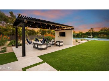 Beautiful backyard patio features a covered lounge area, green lawn, and a luxurious tennis court for outdoor recreation at 8001 E Voltaire Ave, Scottsdale, AZ 85260