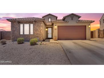 Charming single-story home with stone accents, a two-car garage, and desert landscaping at sunset at 23886 W Harrison Dr, Buckeye, AZ 85326
