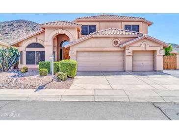 Charming home featuring a tile roof, arched entry, desert landscaping, and a three-car garage at 22019 N 59Th Dr, Glendale, AZ 85310