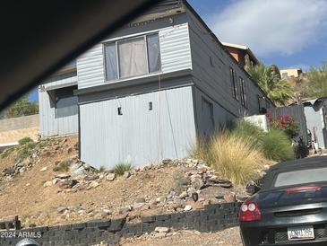View of a gray home on a hillside with sparse vegetation and a black convertible parked nearby at 13024 N 18Th Pl, Phoenix, AZ 85022