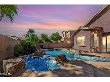 Backyard pool with rock features and desert landscaping offers a luxurious outdoor retreat at sunset at 4662 S Calico Rd, Gilbert, AZ 85297