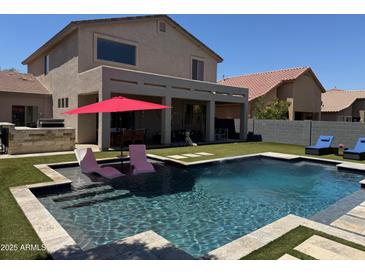 Resort-style backyard featuring pool with baja step, covered patio, and artificial grass at 10430 W Los Gatos Dr, Peoria, AZ 85383