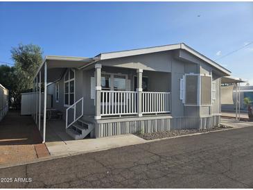 Charming home exterior with covered porch, white railings, and well-maintained landscaping under a clear blue sky at 2121 N Center St # 131, Mesa, AZ 85201