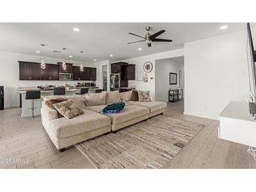 Bright open-concept living room featuring a large sectional couch, modern ceiling fan, and seamless flow to kitchen at 36922 N Camarillo Dr, San Tan Valley, AZ 85140