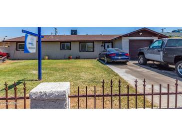 Modest single-story home with a brown roof, a blue car parked on the driveway, and a small fenced front yard at 6063 W Earll Dr, Phoenix, AZ 85033