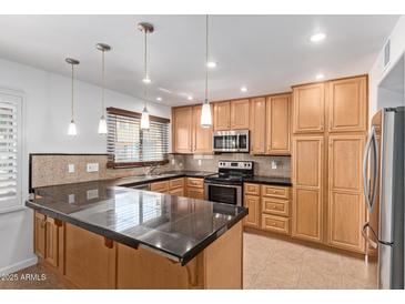 An open kitchen with black countertops, wood cabinets, stainless steel appliances, and stylish pendant lighting at 4629 S Mill Ave, Tempe, AZ 85282