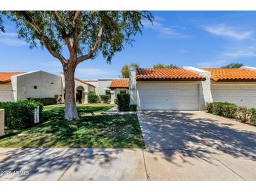 Charming single-story home with a well-manicured lawn, mature shade tree, and a two-car garage with a red tile roof at 9322 E Jenan Dr, Scottsdale, AZ 85260