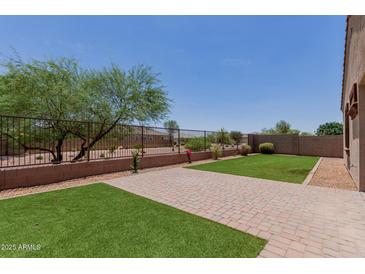 Backyard featuring a well maintained lawn, brick patio, and a metal fence. Tree provides shade, enhancing the outdoor experience at 41041 W Somers Dr, Maricopa, AZ 85138